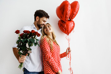 Couple. Love. Valentine's day. Emotions. Man is giving heart-shaped balloons to his woman, both smiling; on a white background