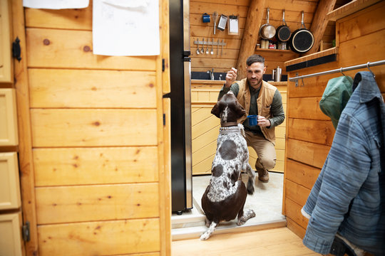 Man Giving Dog A Treat In Cabin Kitchen