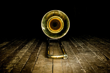 yellow brass instrument trombone lies on the wooden floor of the stage. front view on the bell