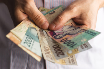man in white shirt counts money in hands. Man hands holding pile of money. counts money in hands. Small Indonesian rupiah money