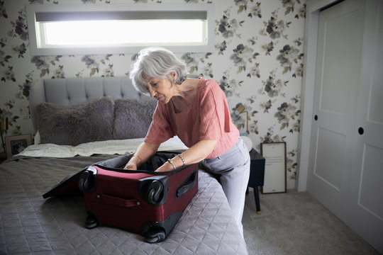Senior woman packing suitcase on bed