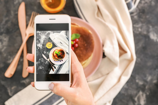 Female food photographer with mobile phone taking picture of pancakes