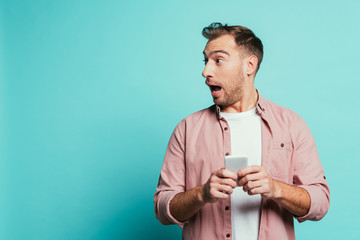 shocked handsome man using smartphone, isolated on blue