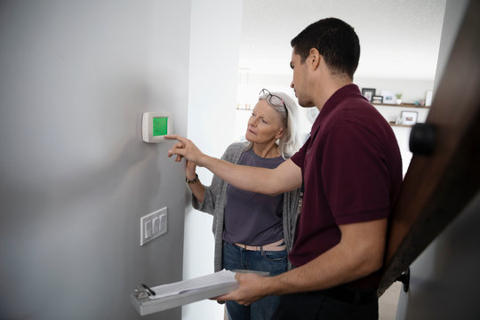 Service technician helping senior woman with digital thermostat