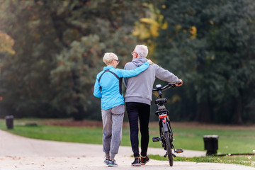 Cheerful active senior couple with bicycle walking through park together. Perfect activities for elderly people.