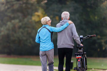 Cheerful active senior couple with bicycle walking through park together. Perfect activities for elderly people.