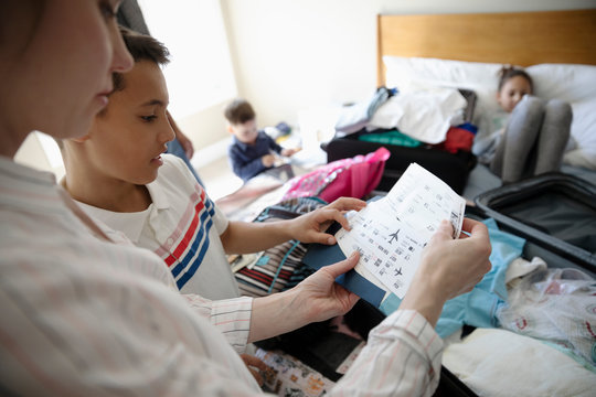 Family with airplane tickets packing suitcases for vacation on bed