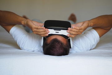 A man is watching a 3D video in a virtual reality helmet lying on the bed.