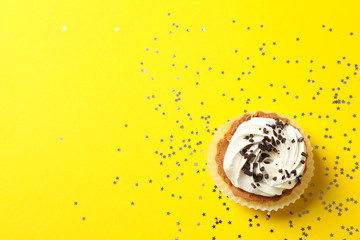 Cupcake and glitter stars on yellow background, top view