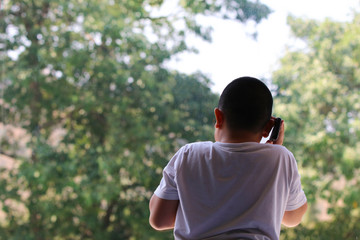 Back of fat boy talking technology smartphone wireless and speaking with someone near window...