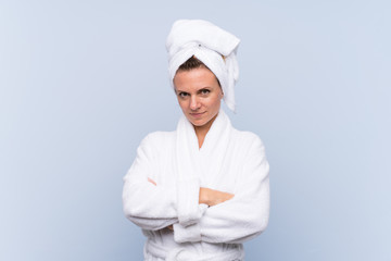 Woman in bathrobe over isolated blue background keeping arms crossed