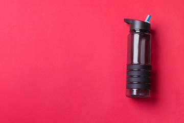 black plastic sport bottle lying on right side of red background with copy space
