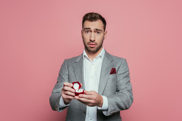 confused man holding box with proposal ring, isolated on pink