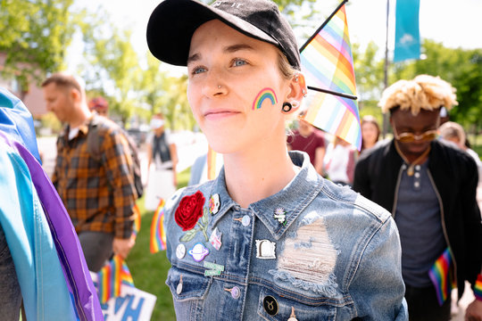 Non binary gender student with rainbow flag on cheek at gay pride festival
