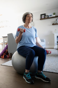 Senior woman exercising with dumbbells on fitness ball in living room