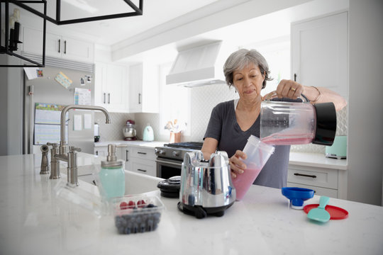 Senior woman making smoothie with blender in kitchen