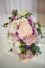 Close up of bridal bouquet of pink, violet and white roses and ranunculus with satin ribbon on mirror table, copy space. Wedding details