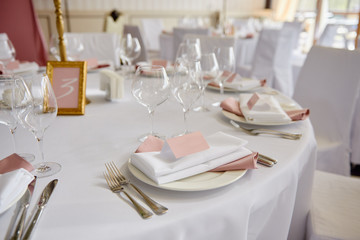 Table set with blank guest card, plate with pink and white serviette and cutlery on table, copy space. Place setting at wedding reception. Table served for wedding banquet in restaurant