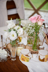 Beautiful floral arrangement of roses and greenery in glass vase on wedding table in restaurant, copy space. Rustic wedding decorations. Table setting