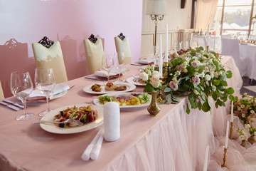 Wedding presidium in restaurant, copy space. Banquet table for newlyweds with flowers, greenery, candles and pink cloth. Lush floral arrangement. Luxury wedding decorations