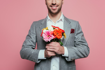 cropped view of happy man holding bouquet of flowers, isolated on pink