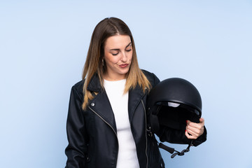 Young blonde woman with a motorcycle helmet over isolated blue background with sad expression