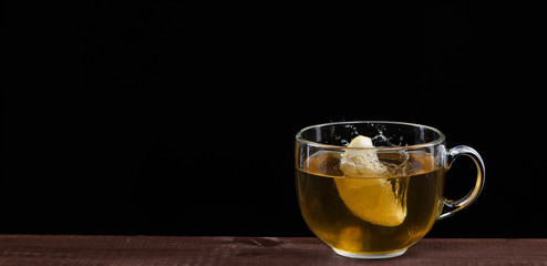 Lemon falls in a mug with tea on a black background with a lot of splashes. Frozen moment