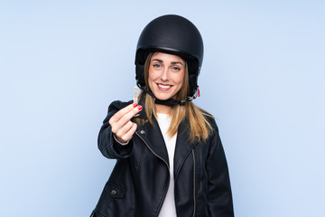 Young blonde woman with a motorcycle helmet and a key over isolated blue background