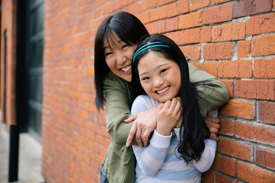 Portrait happy mother and daughter with down syndrome hugging at brick wall