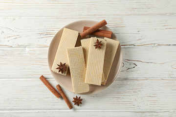 Plate with wafers and cinnamon on white wooden background, top view