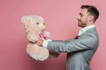 cheerful man in suit holding teddy bear on pink