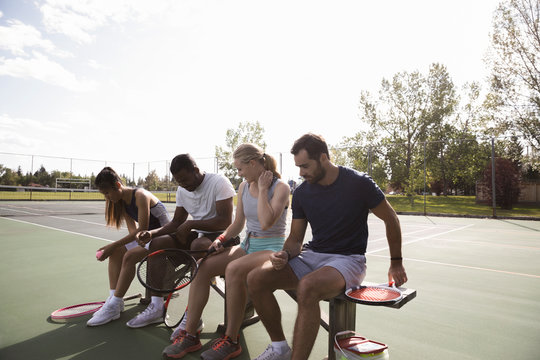 Young couples preparing to play tennis on sunny tennis court bench