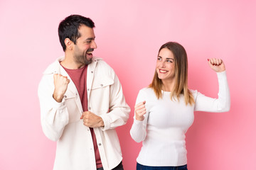 Couple in Valentine Day over isolated pink background celebrating a victory in winner position