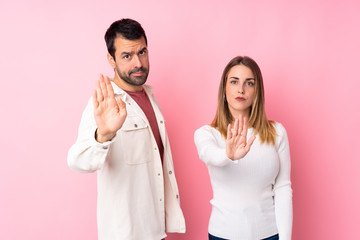 Couple in Valentine Day over isolated pink background making stop gesture denying a situation that...