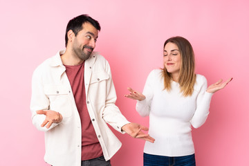 Couple in Valentine Day over isolated pink background making unimportant gesture while lifting the shoulders