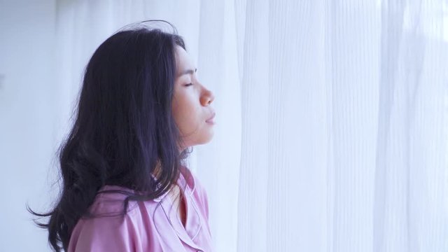 Depressed woman takes deep breath near the window