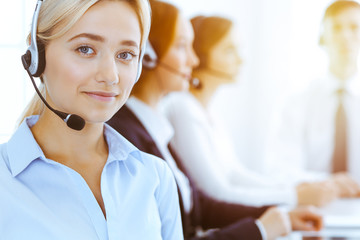 Group of diverse phone operators at work in sunny office. Handsome business woman with headphones...