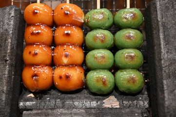 Green and orange colored japanese sweets on wooden sticks on a market in Osaka-Japan.