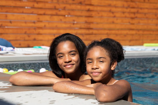 Portrait smiling, confident sisters at the edge of sunny, summer swimming pool