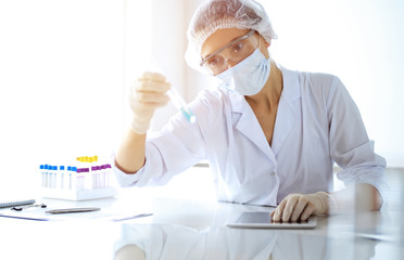 Professional female scientist in protective eyeglasses researching tube with reagents in sunny...