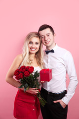 Attractive young woman in dress holding red roses and handsome man in suit are in love