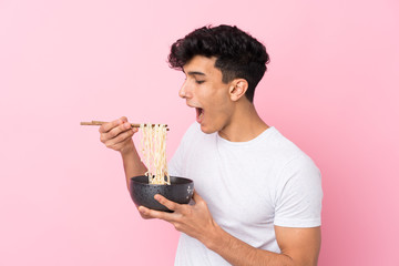 Young Argentinian man over isolated white background holding a bowl of noodles with chopsticks and eating it