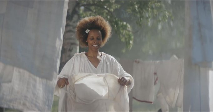 Afro-american female villager hanging laundry outdoors. Historical reconstruction of slavery episodes. 19 century. North America, Southern States