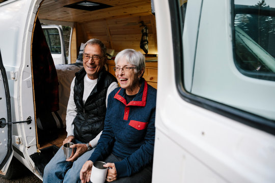Happy senior couple relaxing, drinking coffee at camper van