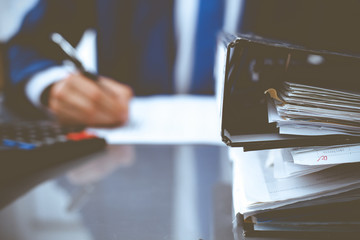 Binders with papers waiting to be processed with businessman or bookkeeper back in blur. Accounting planning budget. Audit, insurance and business concept