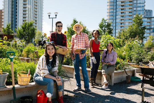 Portrait Happy Man Teaching Gardening To Young Adults In Sunny, Urban Community Garden