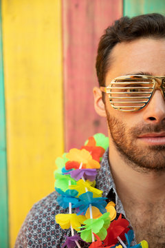 Close up portrait playful, cool young man wearing lei and golden sunglasses on summer patio