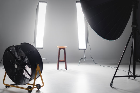 digital camera, fan, reflector, wooden stool and lights on backstage in photo studio