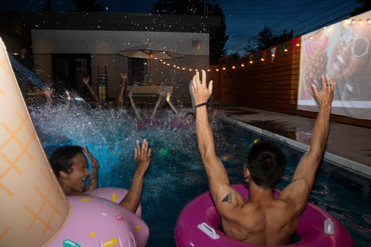 Friends cheering, splashing in summer swimming pool at night