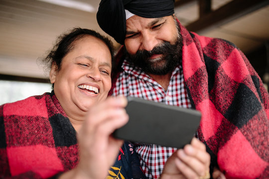 Mature Indian couple wrapped in blanket using smart phone